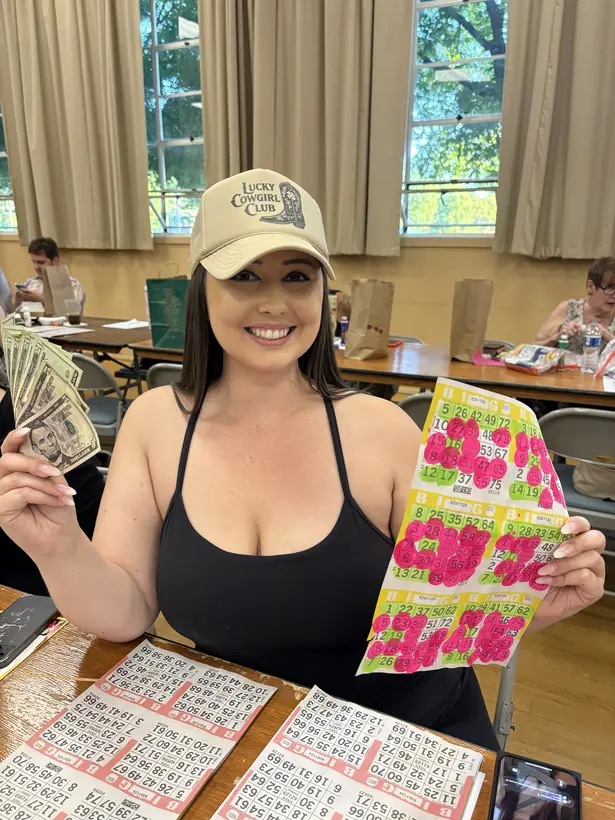 A Wine Country Bingo player holding a bright marked card and cash.