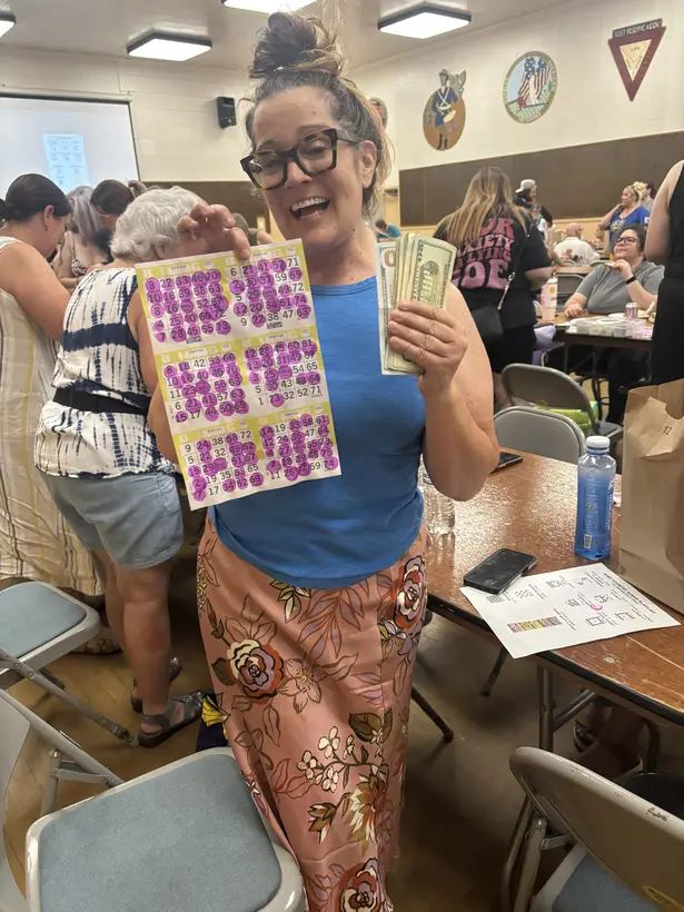 A Wine Country Bingo winner standing among players with her marked card and prize.