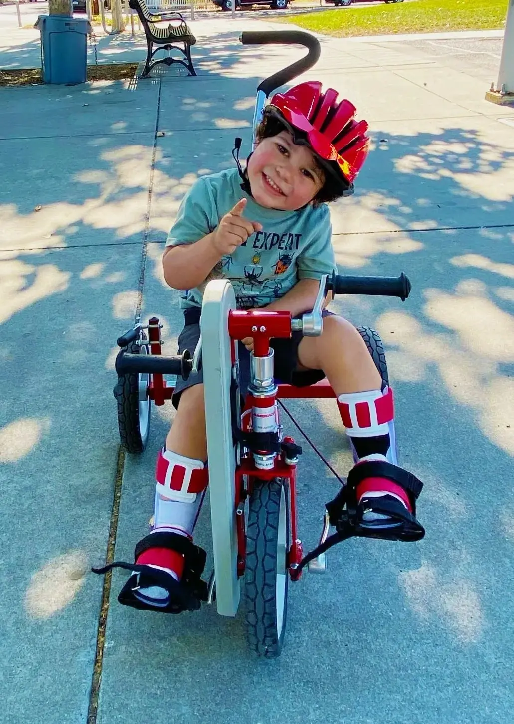 An older Lukas smiling while seated on his red adaptive Tryke.