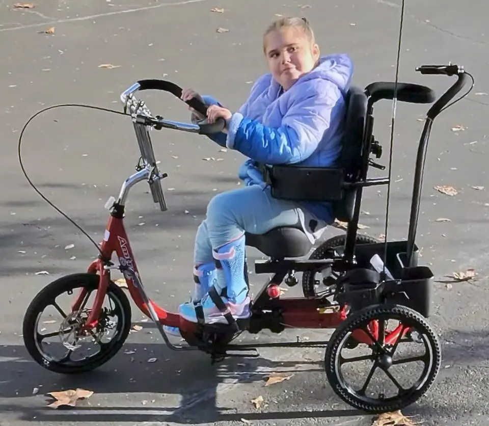 A rider seated on a complete red adaptive tricycle outdoors.